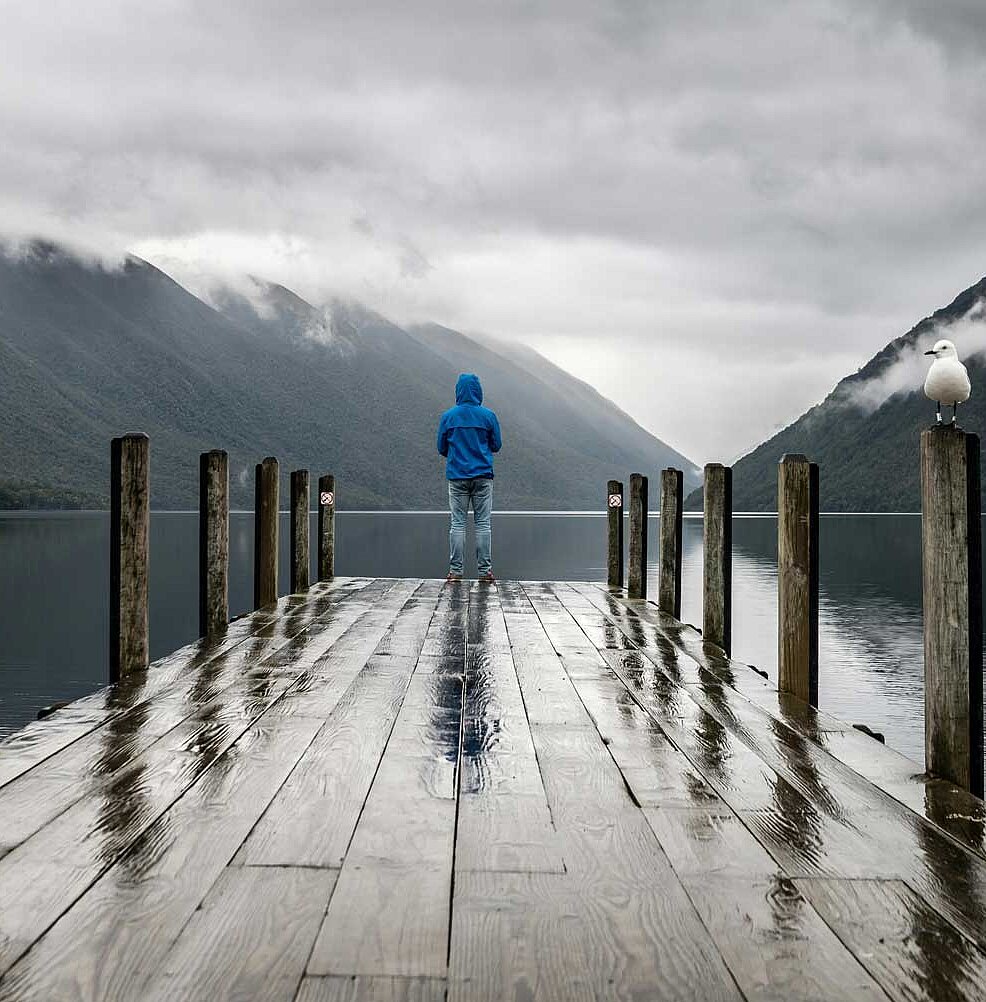 Steg an einem See. Am Ende steht eine Person und schaut auf das Wasser. 