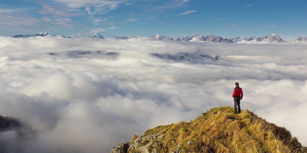 Wanderer steht auf Berggipfel über den Wolken, Schweizer Alpen