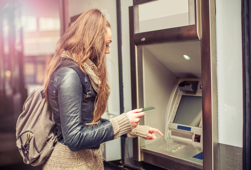 Junge Frau hebt Geld am Automaten ab.