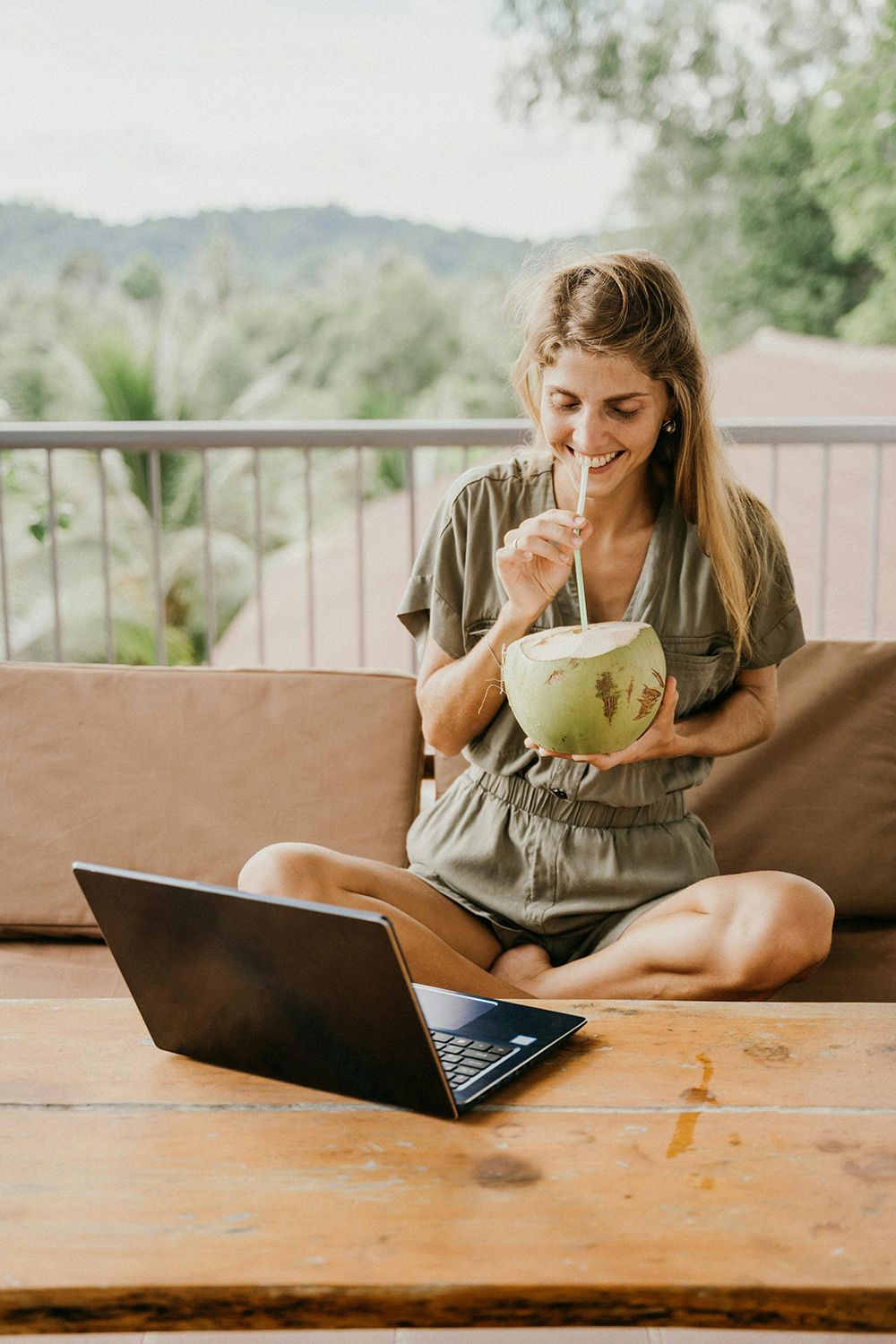 Frau arbeitet an einem Laptop und trinkt einen Kokosnuss 